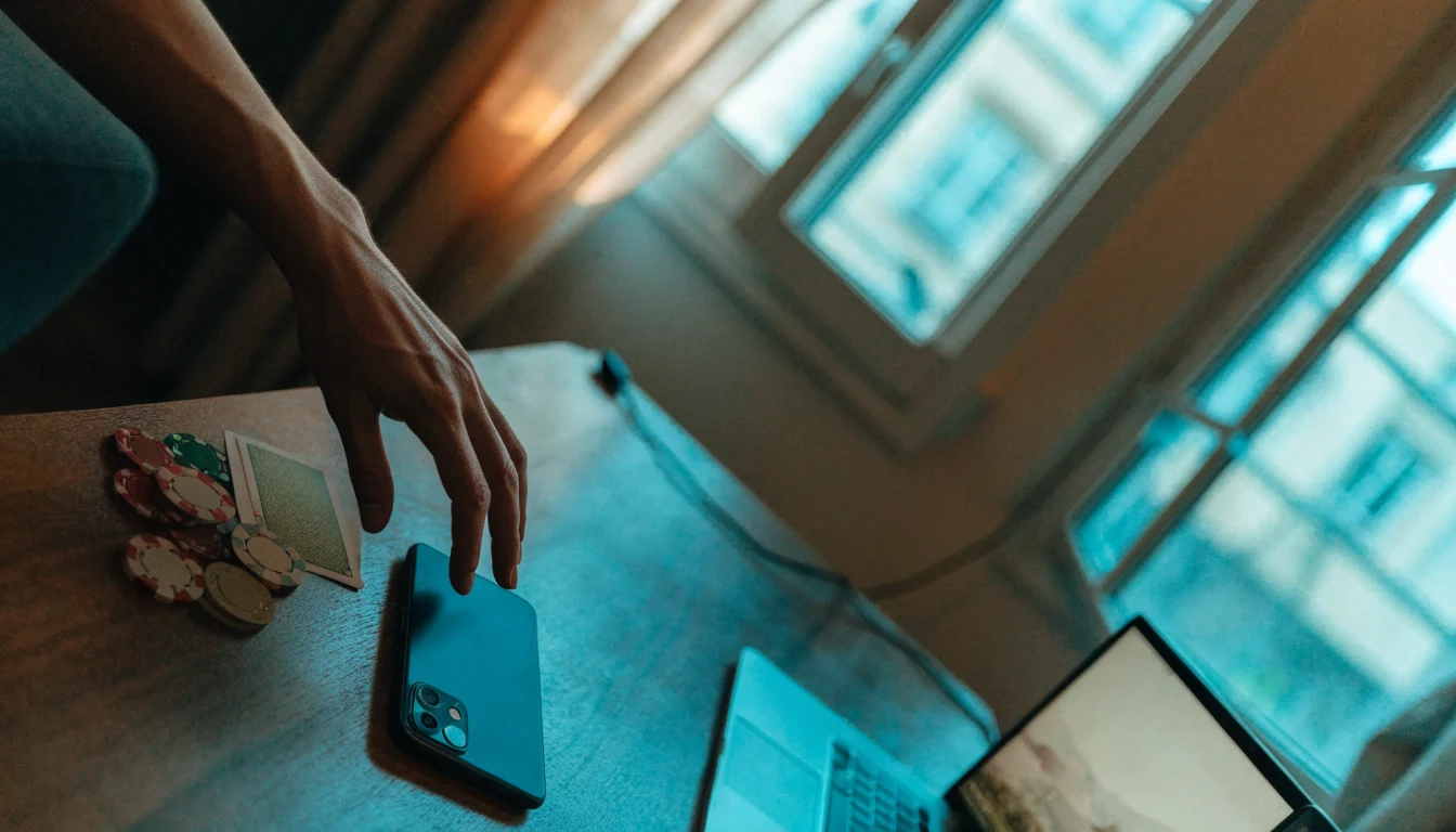 Hand nära en mobiltelefon vid casinokort och marker på ett skrivbord